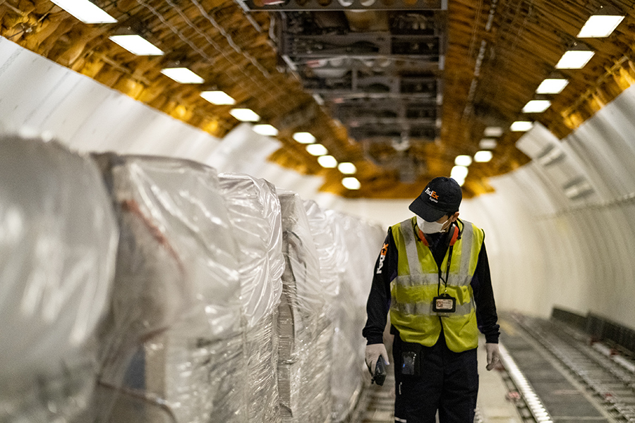 FedEx employee in high-vis vest and mask inspects cargo load