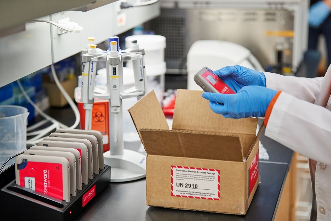 Person in a lab coat places FedEx SenseAware device into package