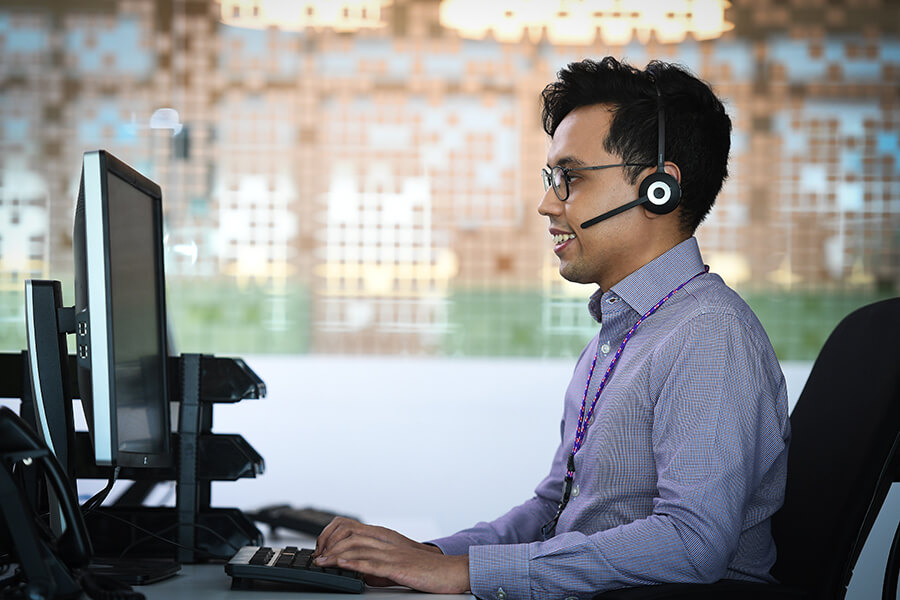 Male customer service agent in headset smiles at computer screen