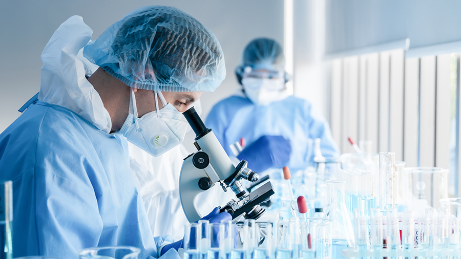 Healthcare professionals in gloves and gown looking through microscope