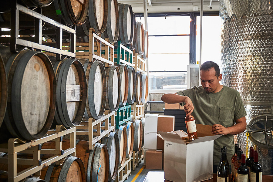 Man packs wine into box next to barrels in winery