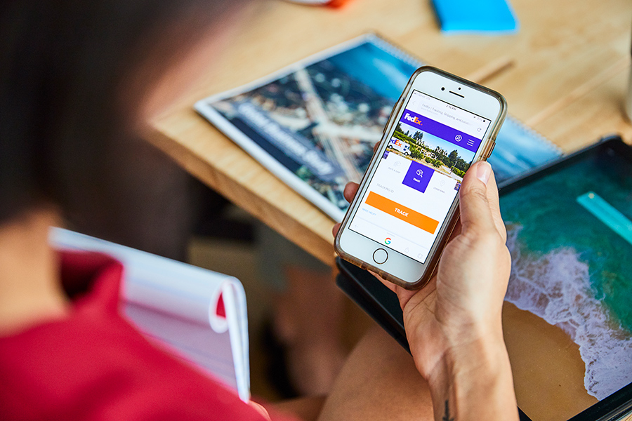 Hand holds mobile screen showing FedEx website