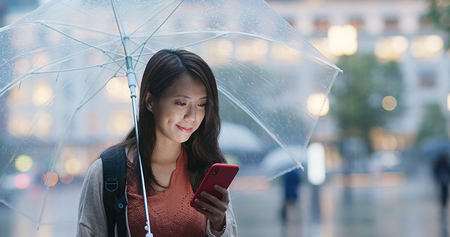 East Asian female smiles at phone screen under umbrella