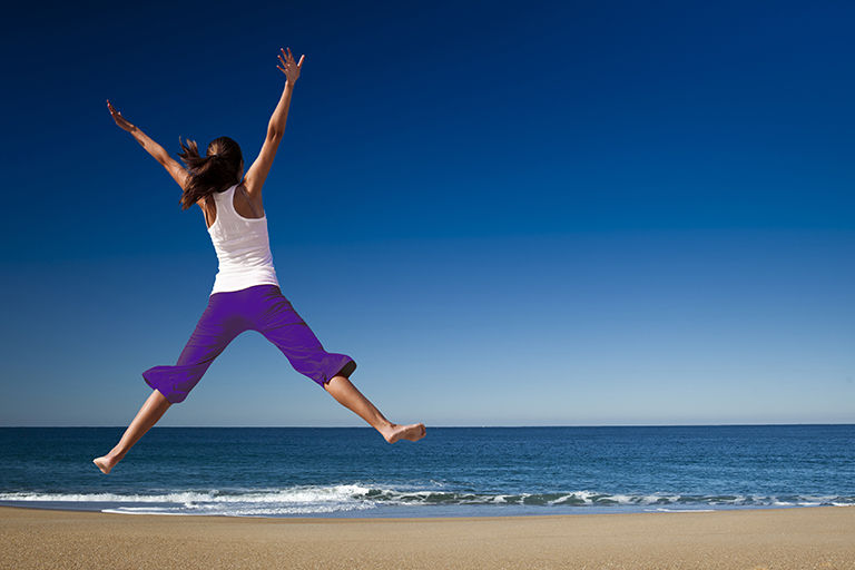 Woman doing star jump on a beach