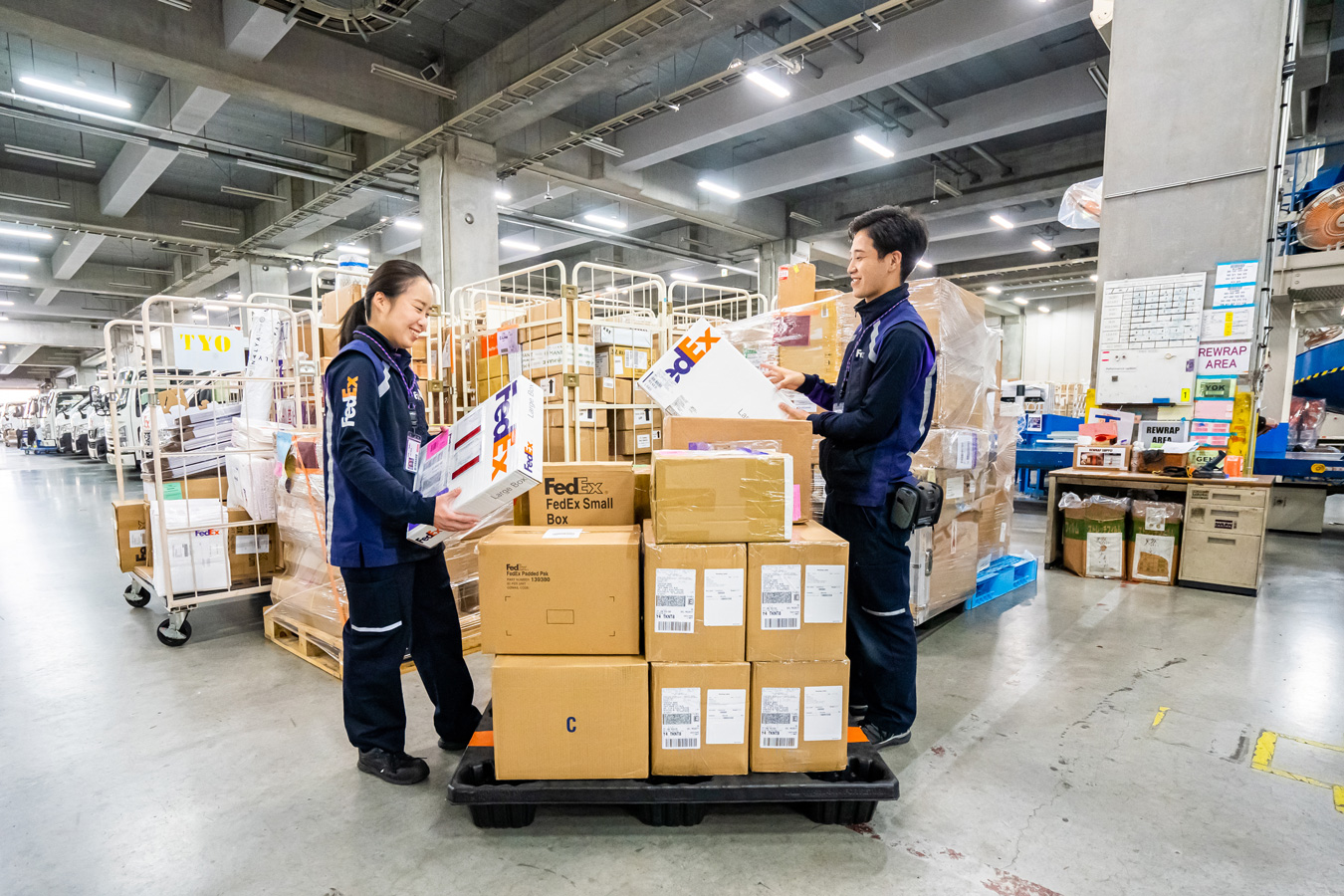 Male and female worker in FedEx uniform stack packages on trolley