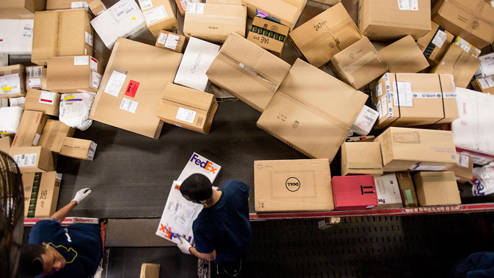 Two male couriers sort large number of FedEx boxes and packages