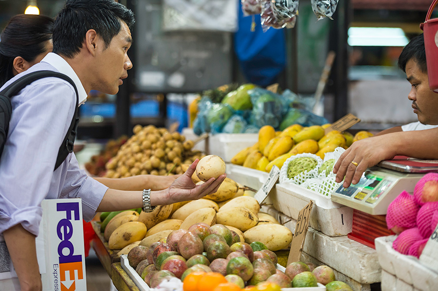 Asian male at fruit stall with FedEx parcel under arm