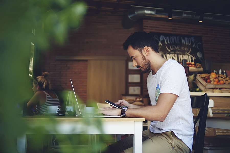 Man using laptop and mobile phone in café table