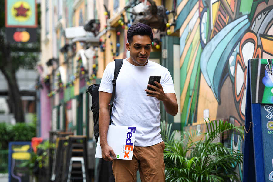 Asian male walks down graffitied side-street using phone and holding FedEx package