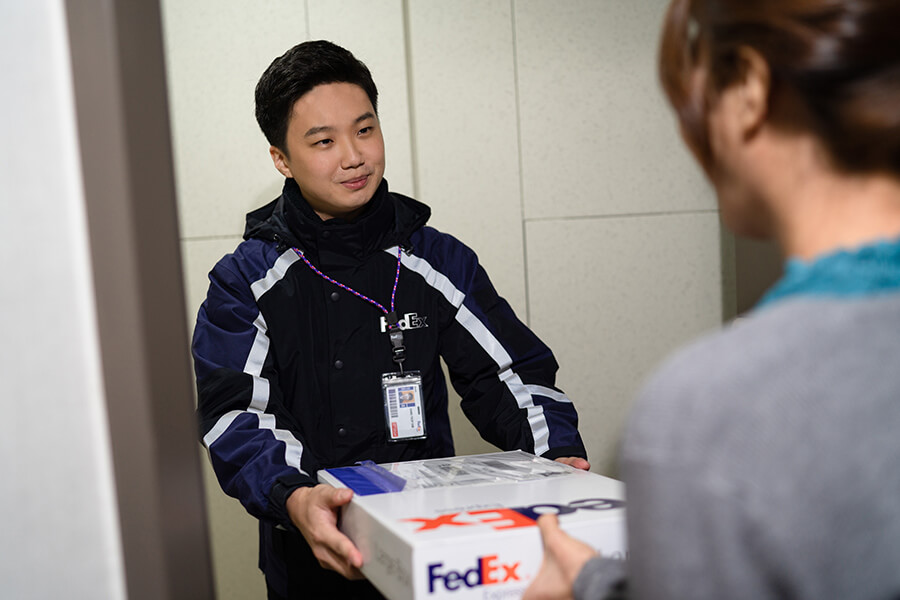 Young male courier hands FedEx parcel to customer in door