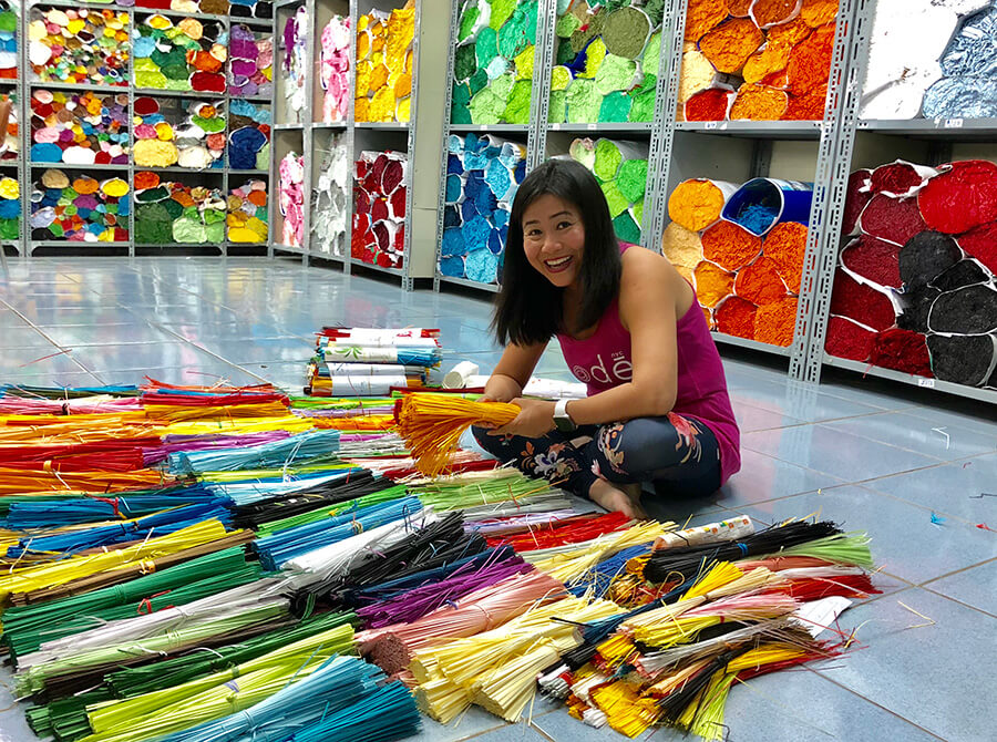 Vietnamese woman sits on floor in fabric warehouse with brightly coloured ribbons