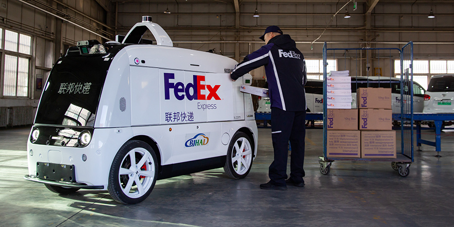 Chinese male courier loads FedEx boxes into white autonomous delivery vehicle