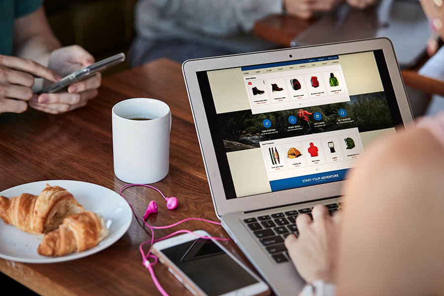 Female browses online clothes shops with coffee and croissant
