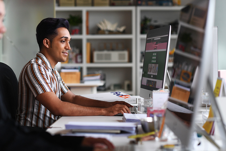 South Asian male works at desk on Apple computer