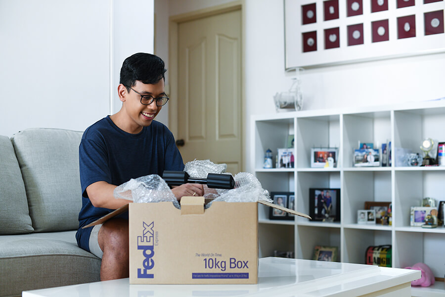 Asian male with glasses opens FedEx box in living room