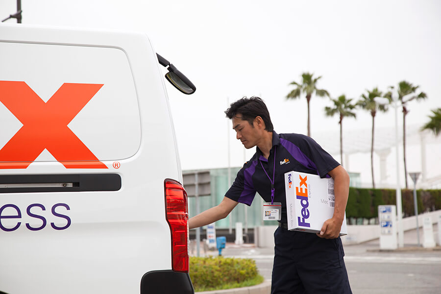 Asian male FedEx courier loading parcel into FedEx van