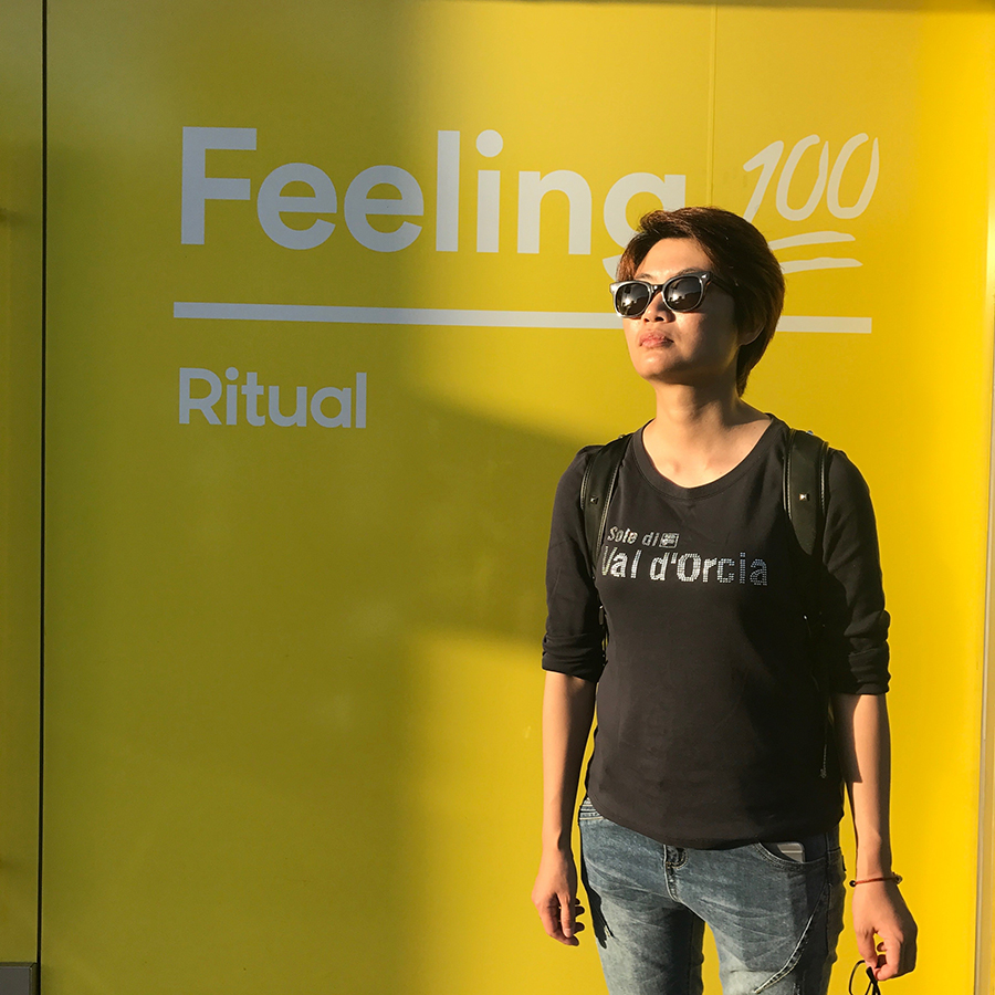 Chinese woman with short hair and sunglasses stands in front of billboard