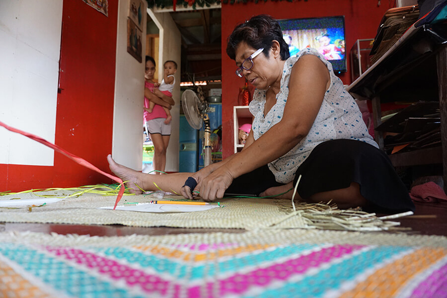 A Filipino mother crafting patterns on a “banig”