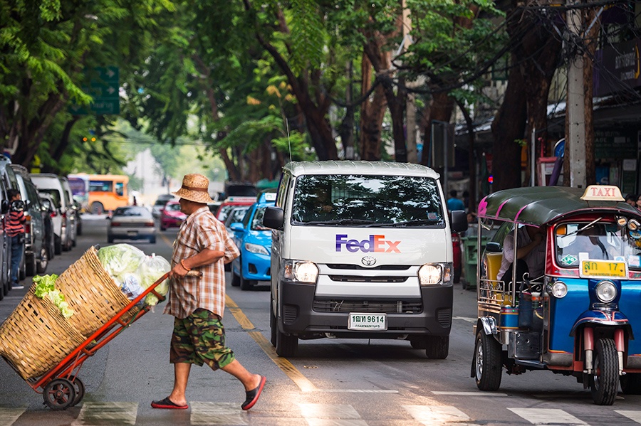 Man crosses Thai street with trolley in front of FedEx van and tuk-tuk