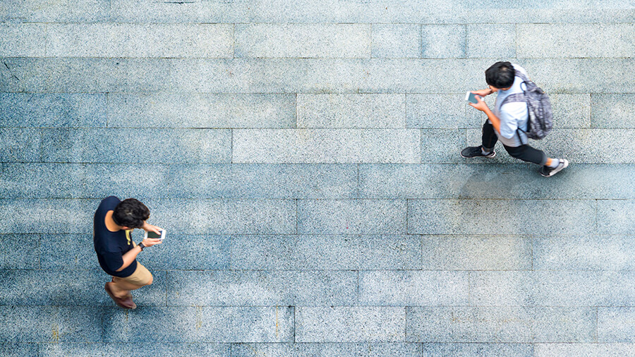 Two men using mobile phones while walking