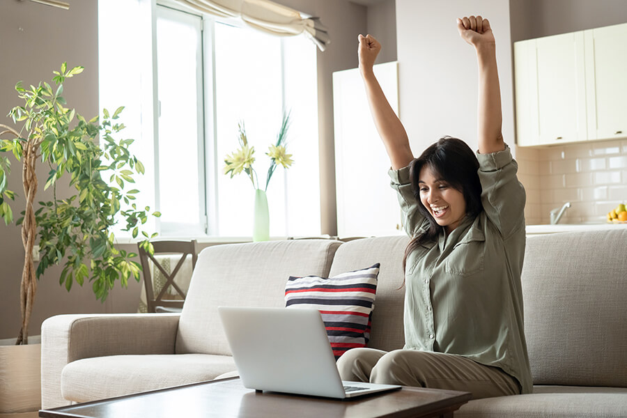 Young Asian female on sofa celebrating in front of laptop