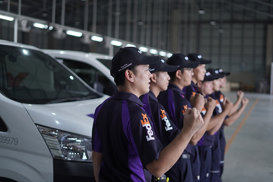 Line of male FedEx couriers in front of vans at depot