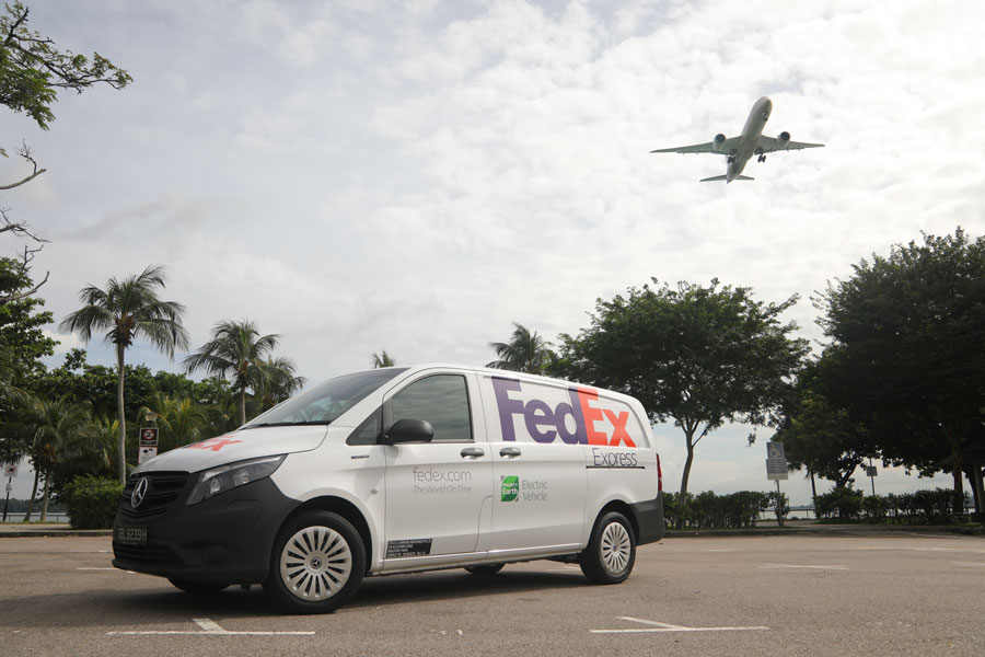 FedEx EV van in car park with plane flying overhead
