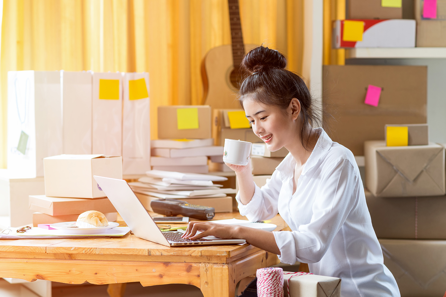 Smiling East Asian female SME working at desk with coffee