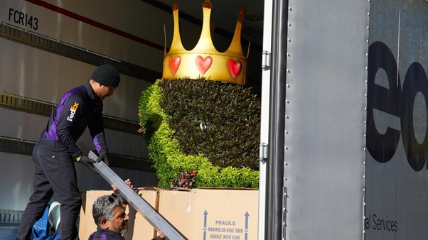 Two male FedEx couriers move large plants from back of truck