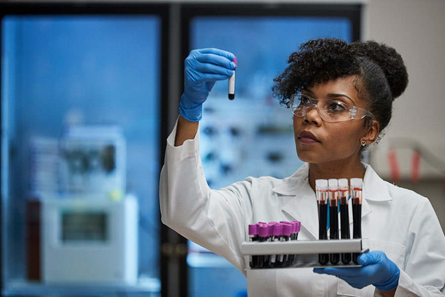 Black female in white lab coat holds up test tubes