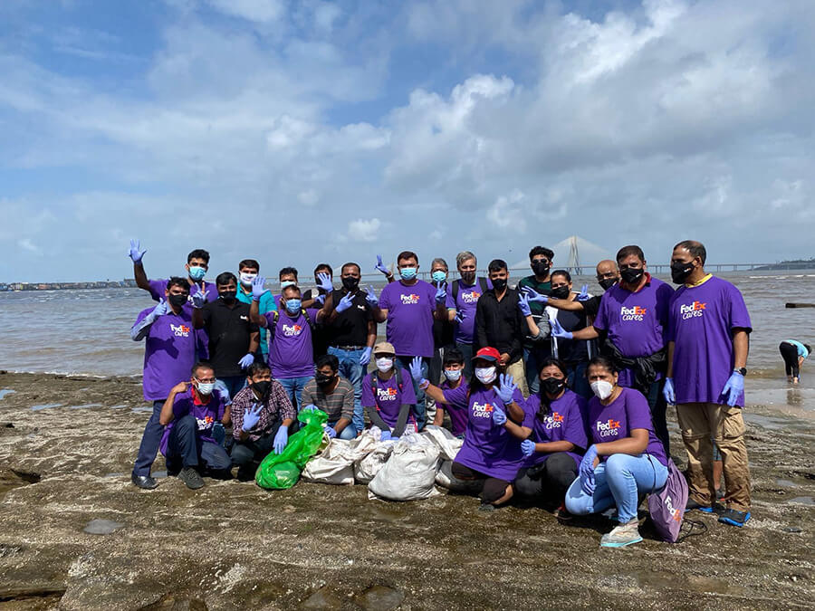 Large group of volunteers in purple FedEx t shirts with full rubbish bags