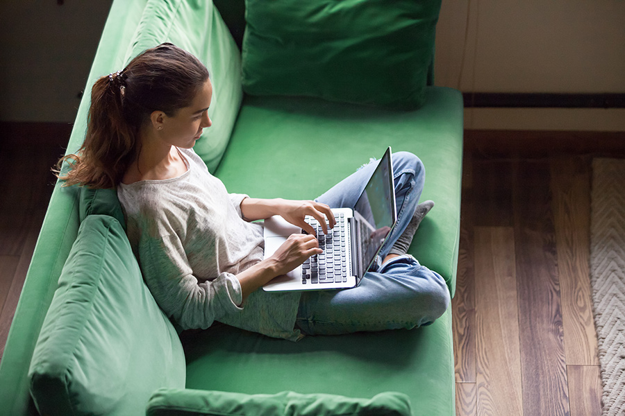 Young female sits cross legged on green sofa with laptop