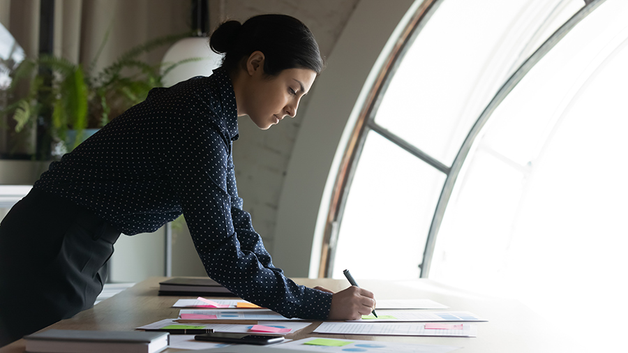 Dark haired female in polka dot shirt draws charts on desk