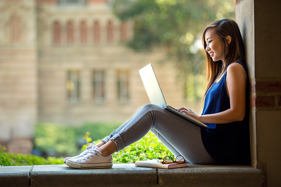East Asian female sits in stone quadrangle with laptop on lap