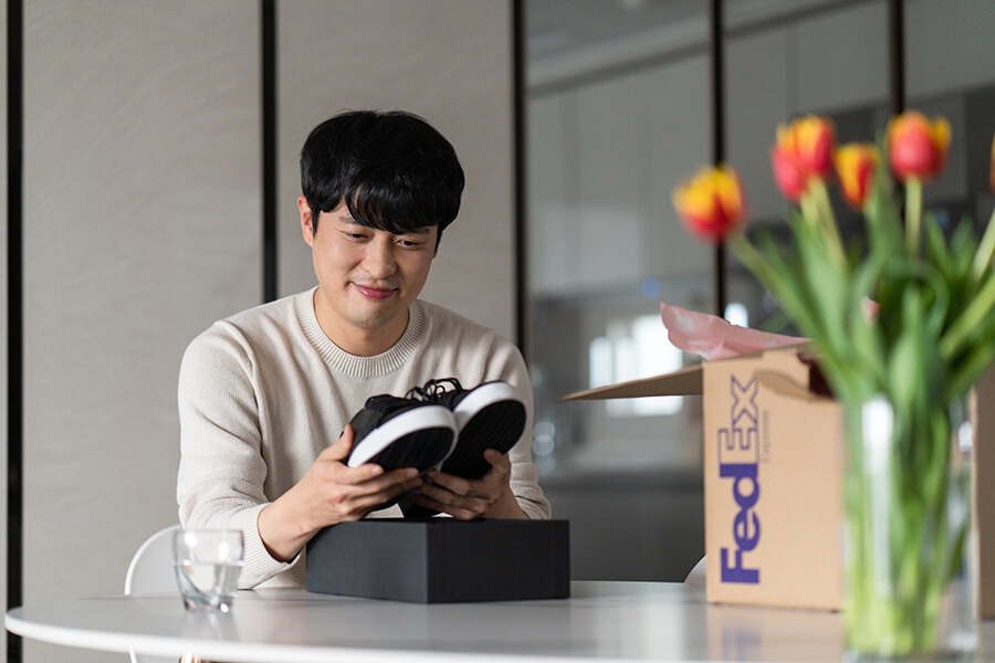 A man unpacking his parcel of a pair of shoes with FedEx box beside him