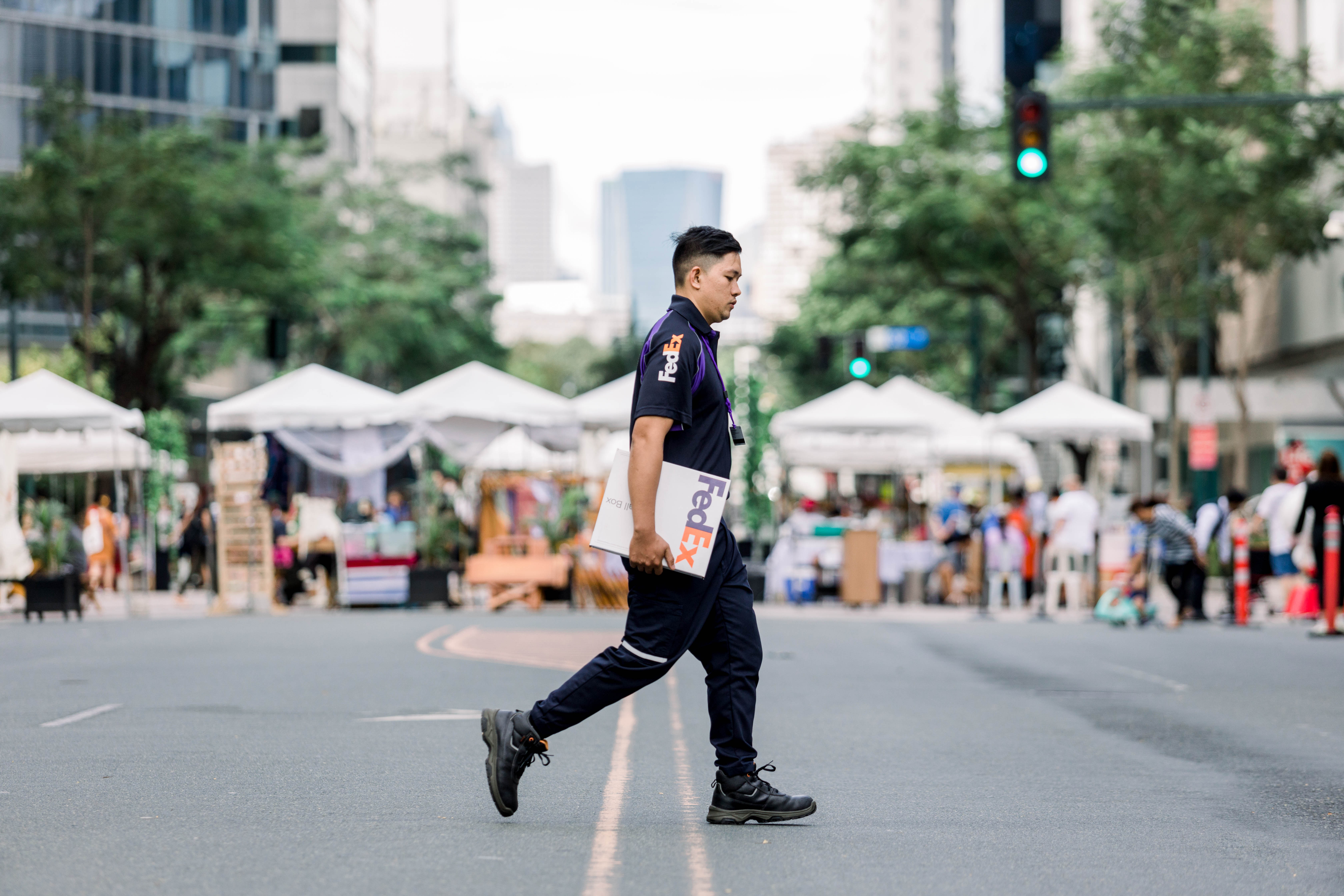 Male Filipino FedEx courier crossing pedestrian area with package