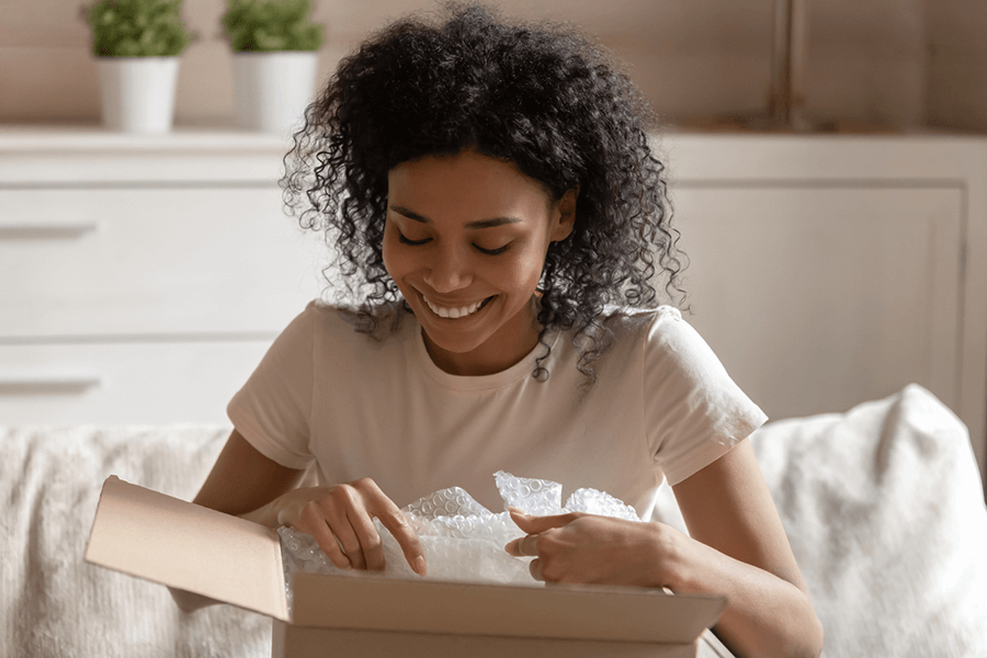 A smiling woman opens a package in her room