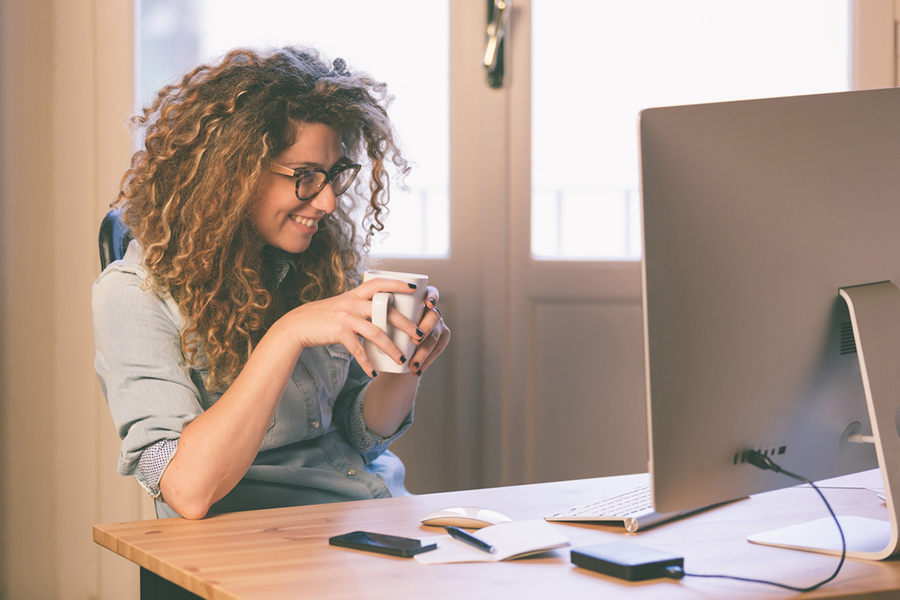Business owner smiling at her personal computer while drinking coffee