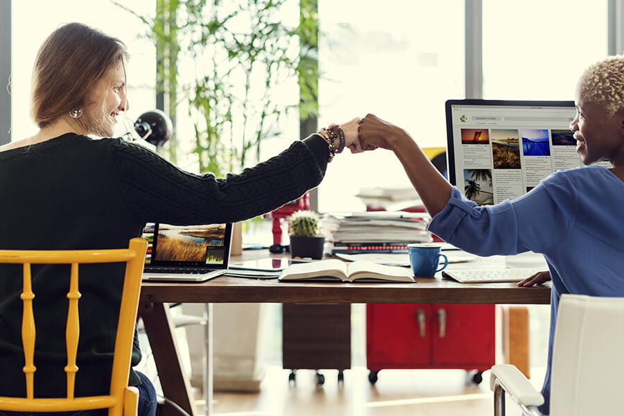 Two women fist bump each other at their work desk