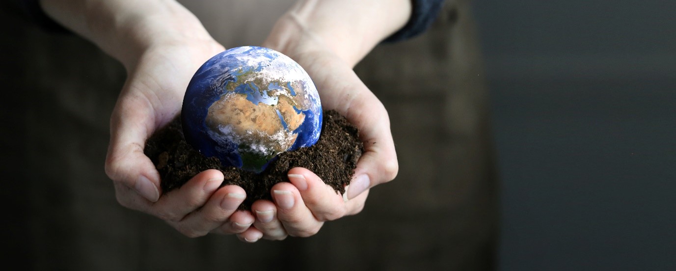 A person holding a small planet with soil in outstretched hands