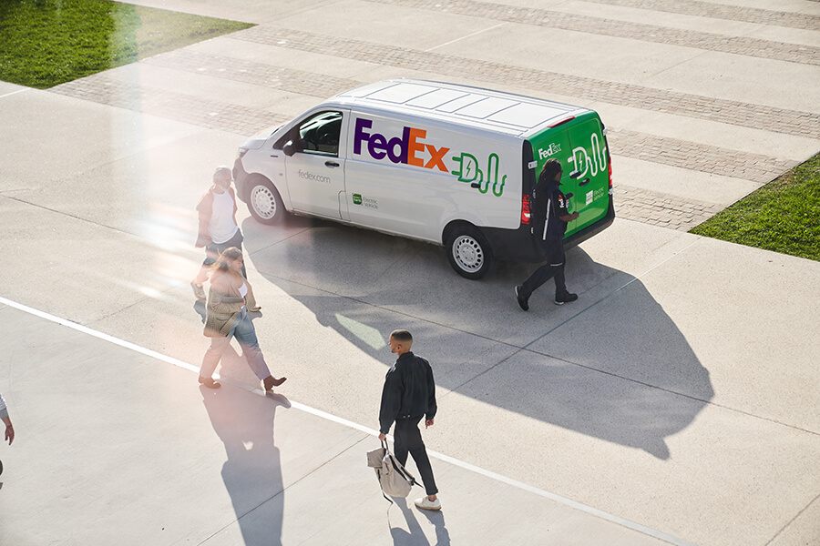 FedEx electric van parked on sunny street with pedestrians
