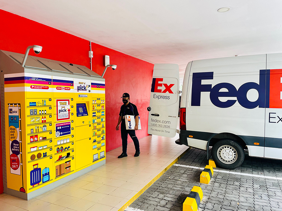 Male FedEx courier drops parcel from van to yellow lockers