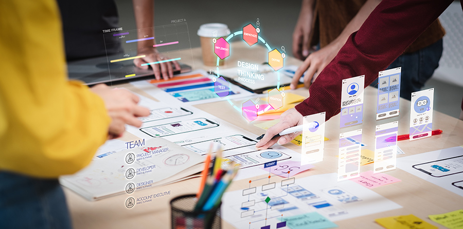 Employees stand around a table with design plans and virtual interfaces