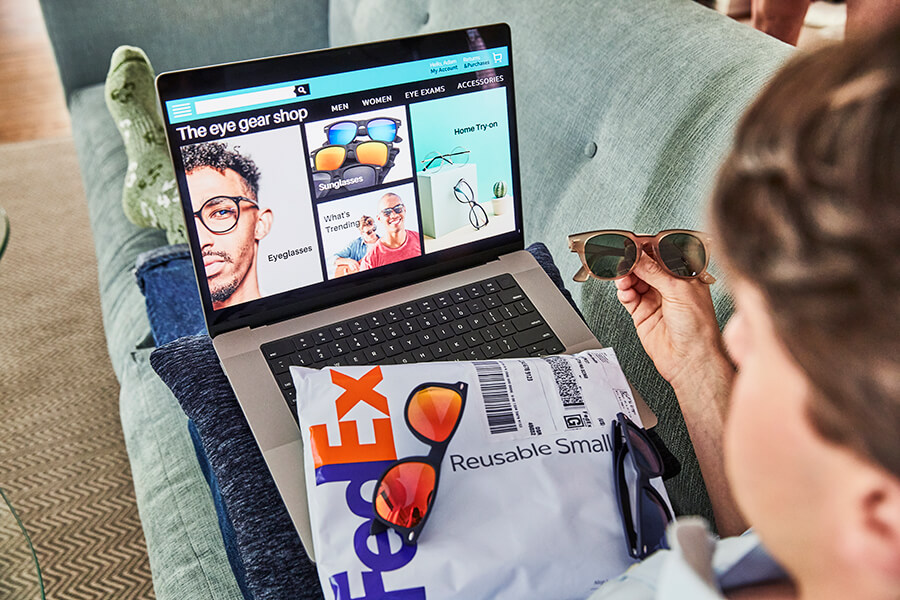 Male online shopper chooses sunglasses on laptop screen with FedEx Reusable Pak on lap