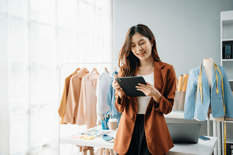 Asian woman standing in a clothing store smiles at a tablet