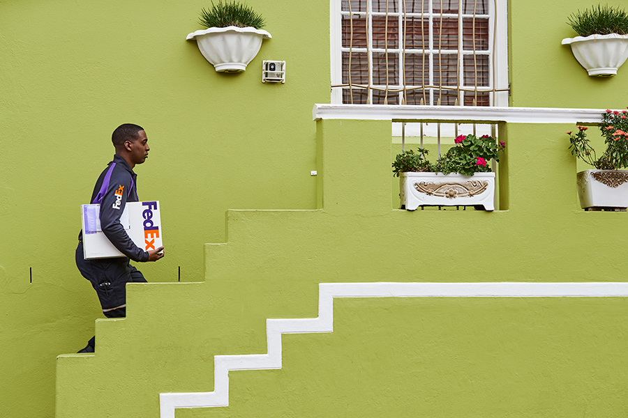 Black male courier delivers FedEx package to a bright green house