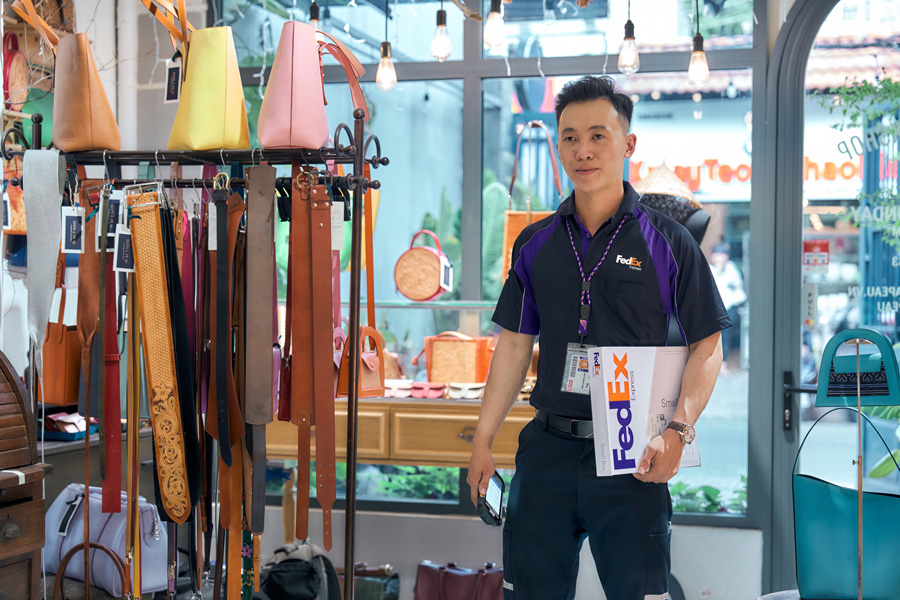 Vietnamese male FedEx courier collects parcel in a fashion retail shop