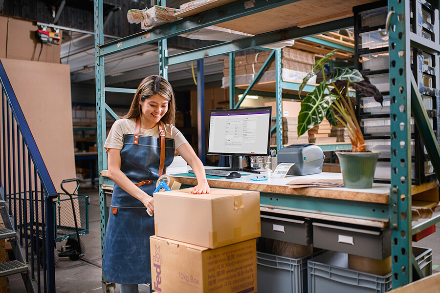 Woman in warehouse in denim overalls packs large FedEx box