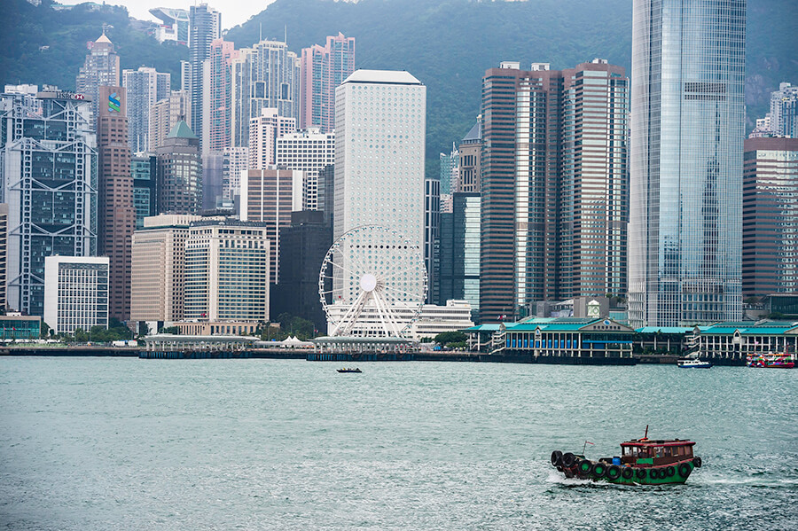 Green sampan boat crosses harbour surrounded by skyscraper buildings