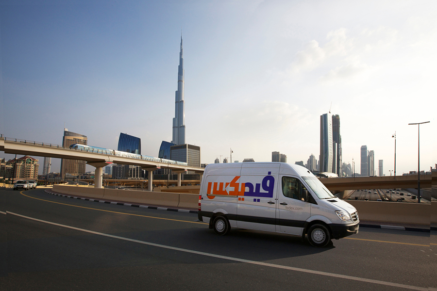 A FedEx delivery van driving on a road in Dubai with the Burj Khalifa and other skyscrapers in the background